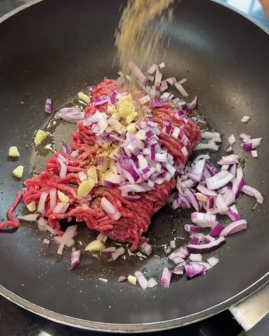 Des épices saupoudrées sur le bœuf haché et les oignons dans une poêle.