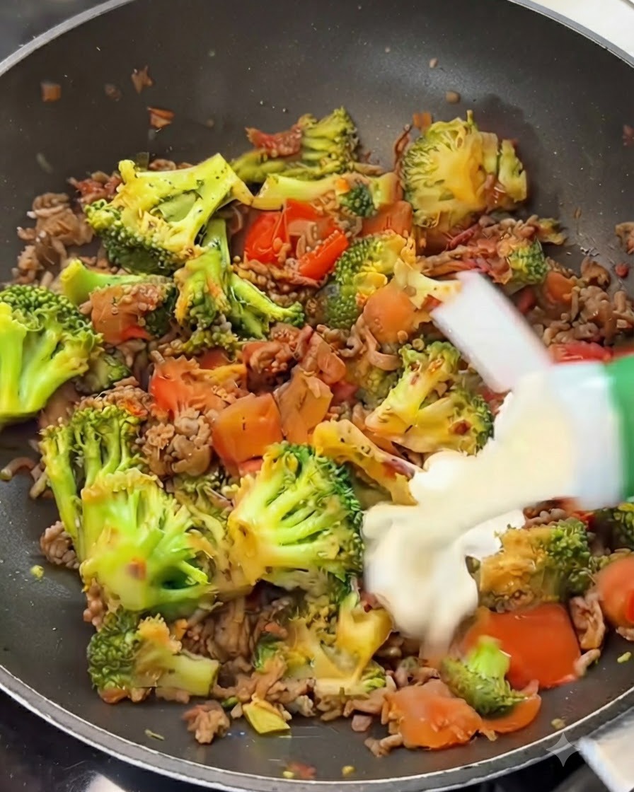De la crème entière versée dune brique sur un mélange de bœuf, de brocoli et de tomates dans une poêle.
