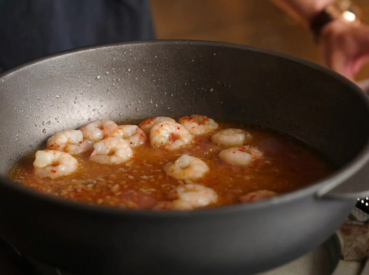 Spaghetti mélangés dans la poêle avec les crevettes, le bouillon et la sauce.