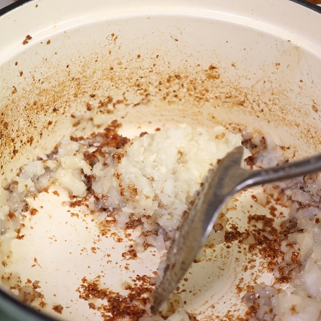 Oignon haché mélangé dans la marmite sur les sucs de cuisson à laide dune spatule.