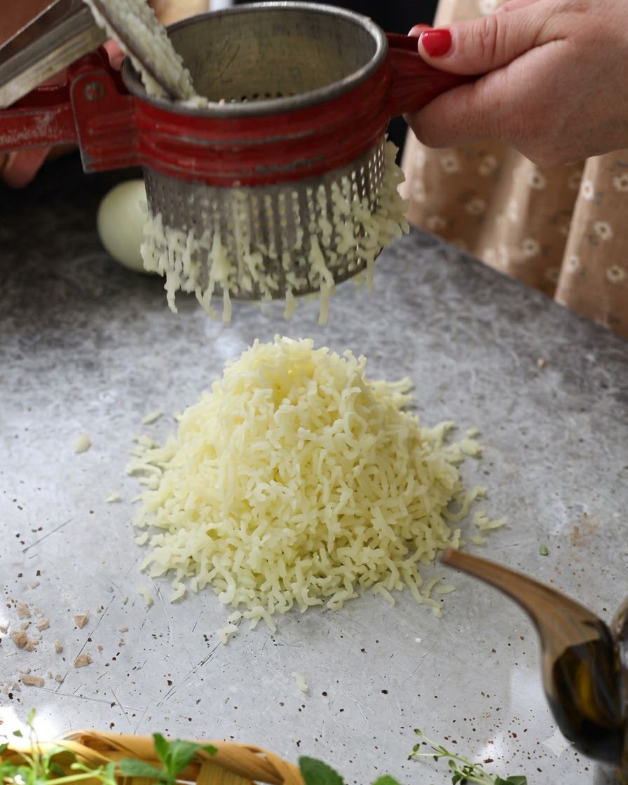 Pommes de terre bouillies chaudes passées à travers un presse-purée rouge pour former un tas moelleux sur la table.