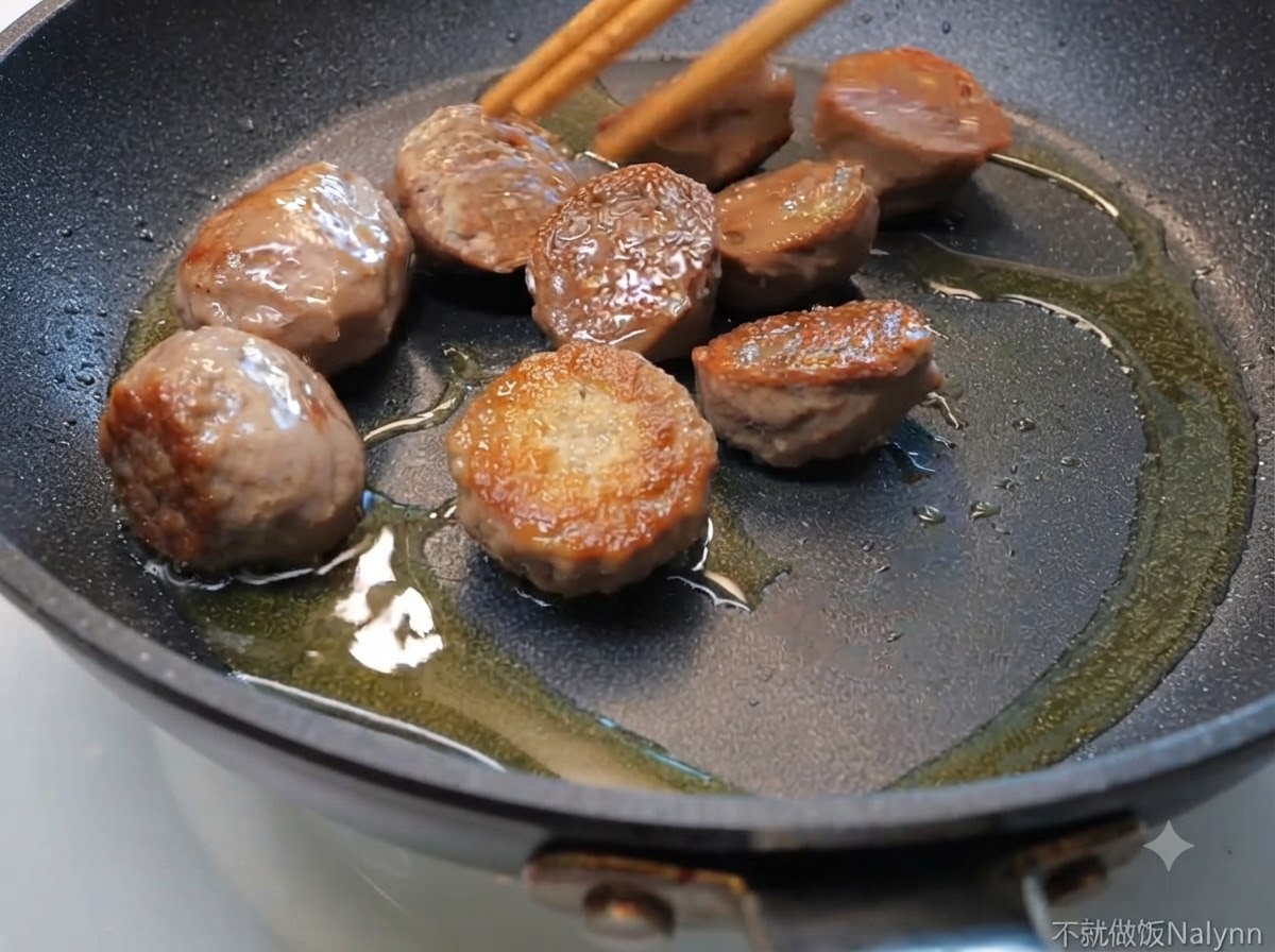 Des moitiés de boulettes de bœuf grésillant dans une poêle avec de lhuile, remuées avec des baguettes en bois.