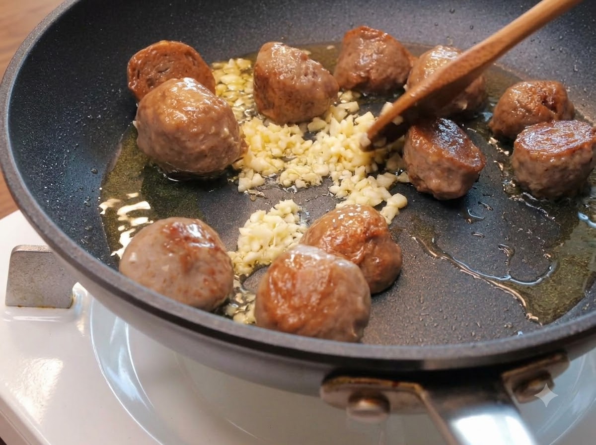 De lail haché éparpillé parmi les moitiés de boulettes de bœuf qui dorent dans une poêle avec de lhuile.