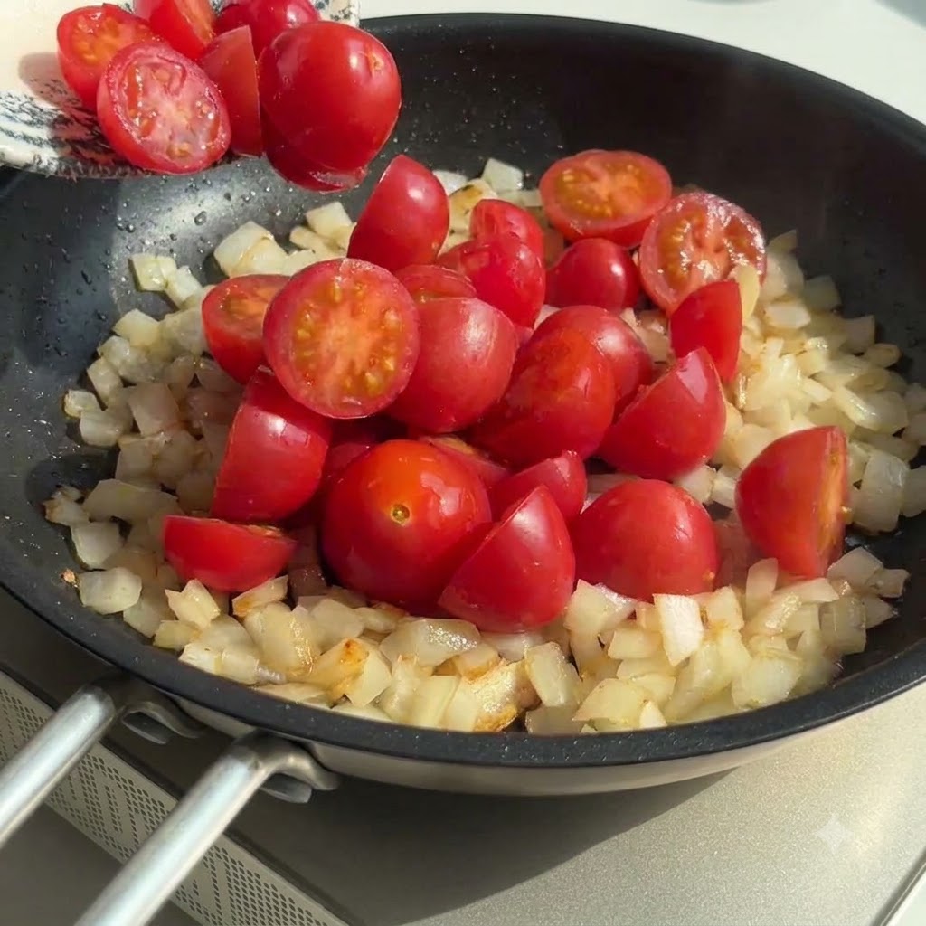 Tomates cerises coupées en deux ajoutées dans la poêle avec les oignons et lail, le tout mélangé.