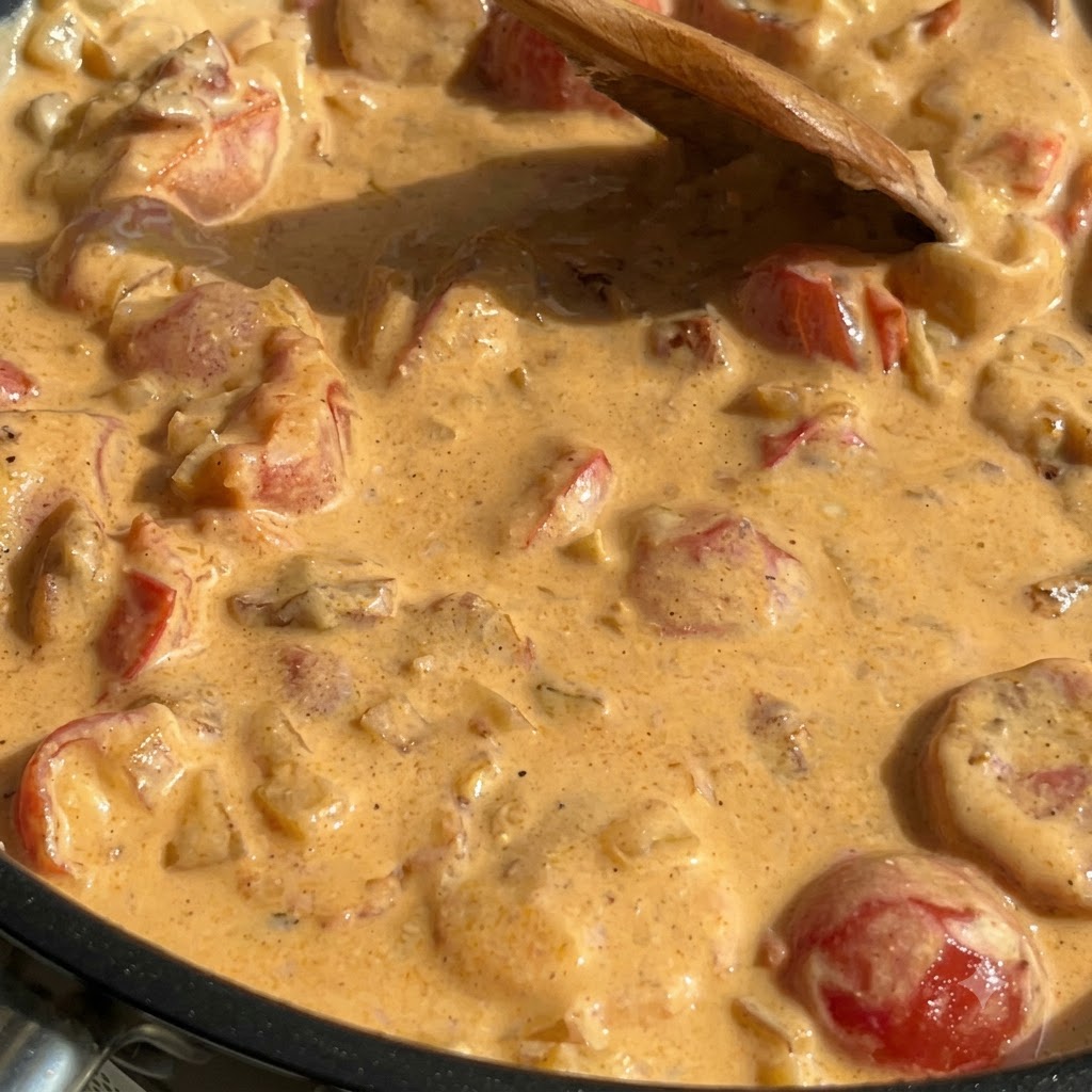 Pâtes cuites, épinards et saumon mélangés dans une sauce crémeuse épaisse à lintérieur dune poêle.