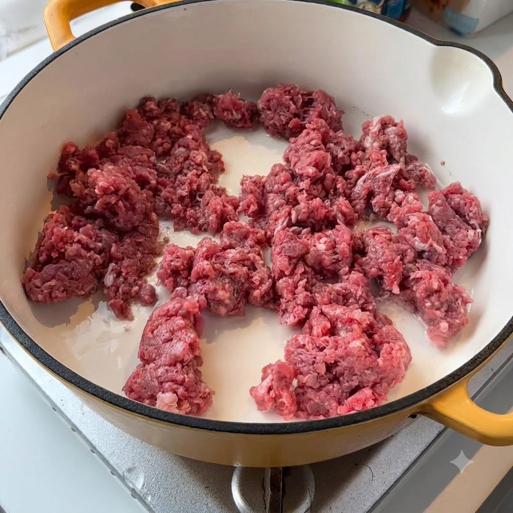 Du bœuf haché cru et des oignons blancs qui grésillent dans une poêle de couleur claire sur la cuisinière.