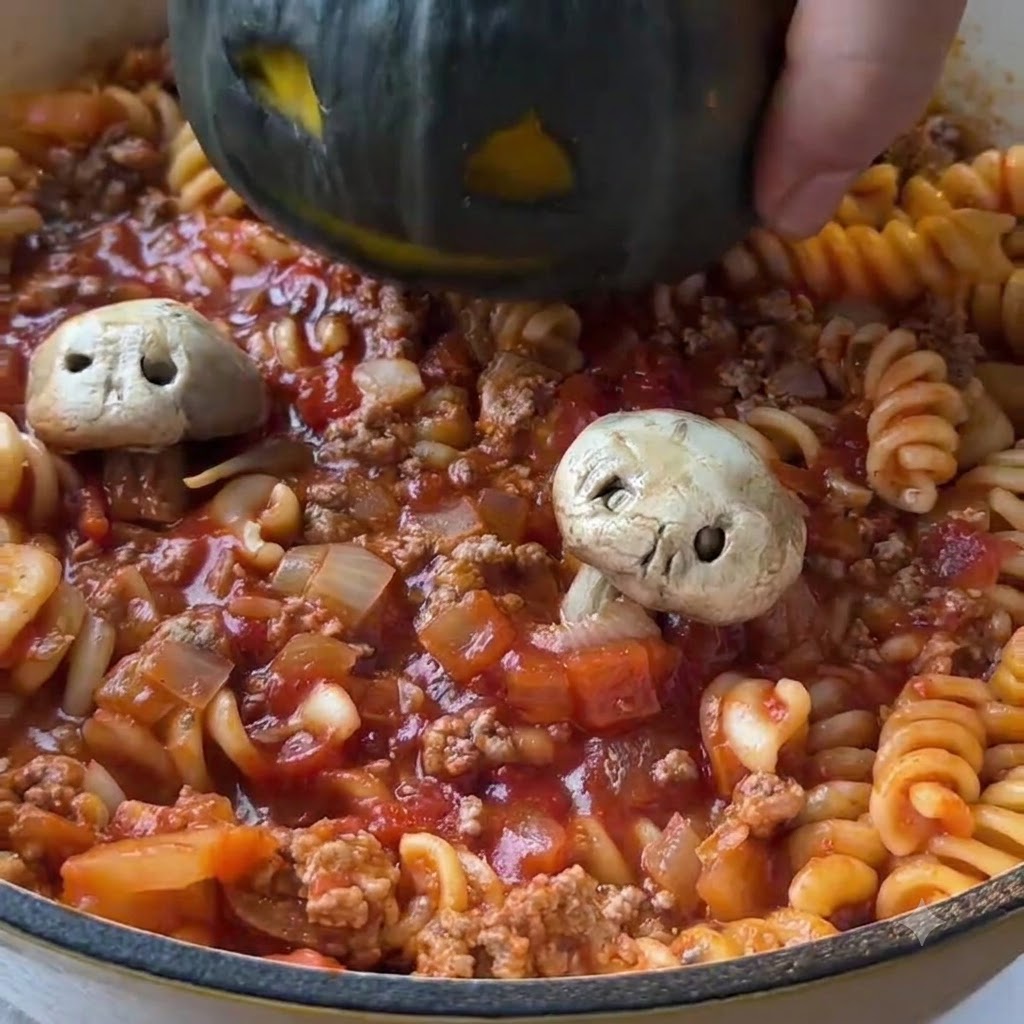 Une mini citrouille vert foncé creusée et sculptée dun visage, abaissée au centre dune poêle remplie de pâtes à la tomate cuites et de sauce à la viande hachée.