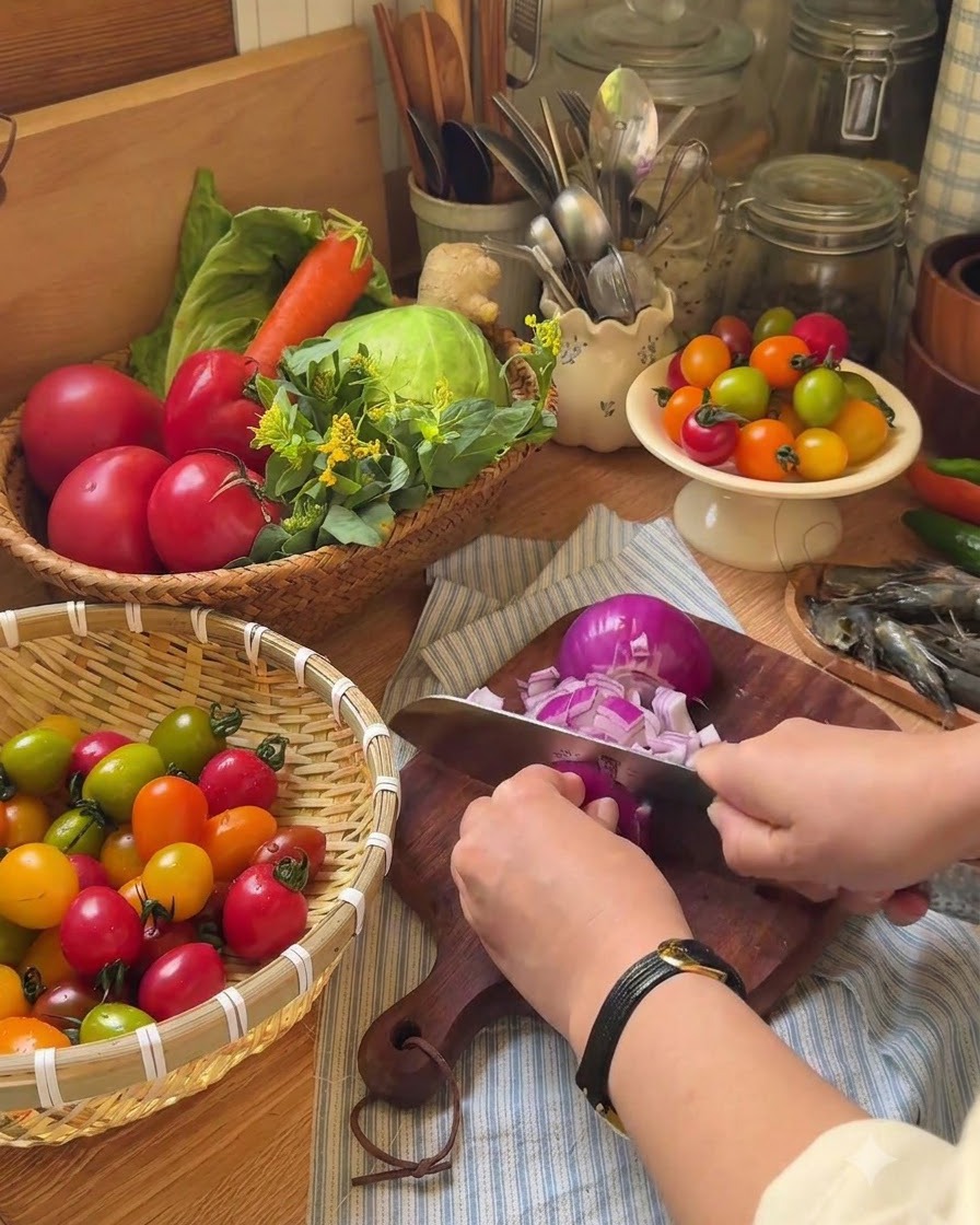 Une main utilisant un couteau pour couper des tomates cerises en deux sur une planche à découper en bois.