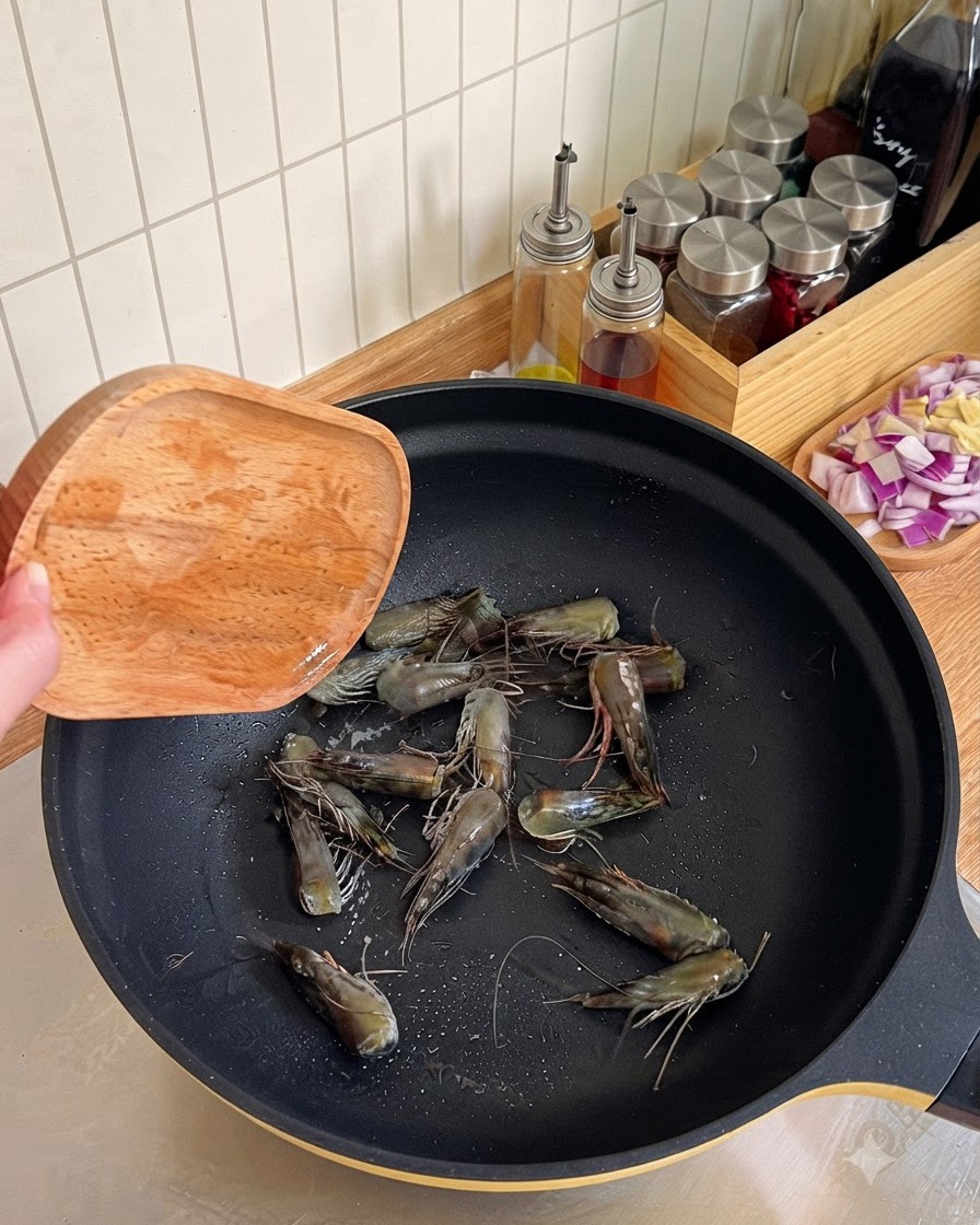 Têtes de crevettes en train dêtre frites et pressées avec une spatule en bois dans un wok noir pour extraire lhuile.