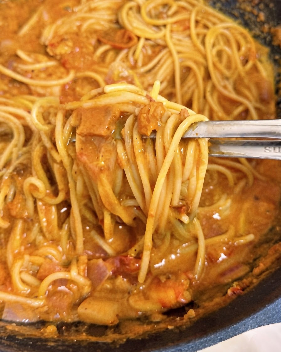 Des pinces soulevant des brins de spaghettis enrobés dune sauce tomate rose crémeuse à lintérieur dun wok.