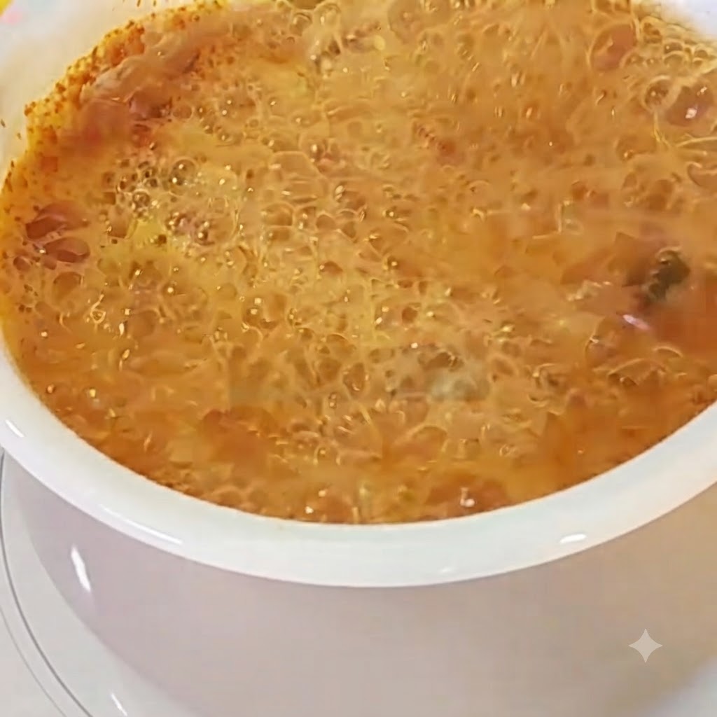 Un œuf cassé dans une casserole de bouillon de ramen rouge bouillant.