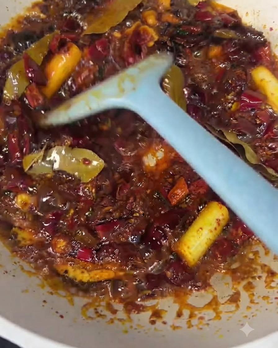 Morceaux de bœuf incorporés dans lhuile pimentée rouge et la base dépices avec une spatule bleue.