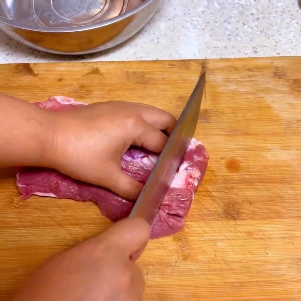 Un couteau de cuisine tranchant du bœuf frais cru en gros cubes sur une planche à découper en bois.