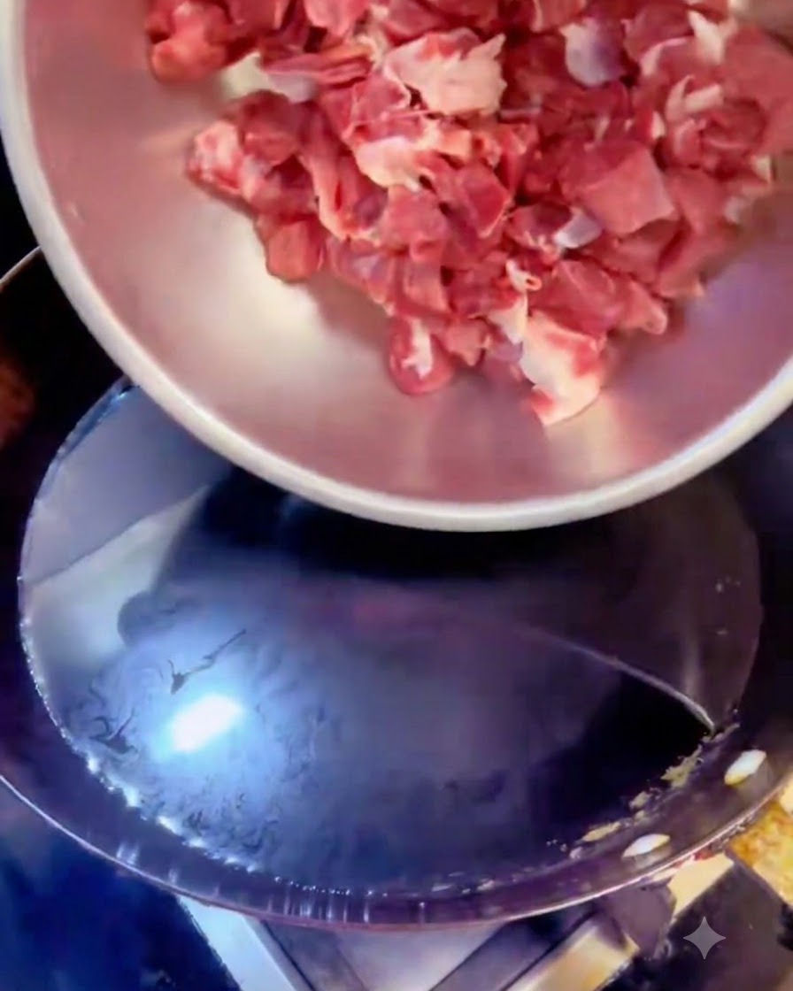 Des cubes de bœuf versés dun bol en acier dans une casserole deau bouillante avec des aromates.