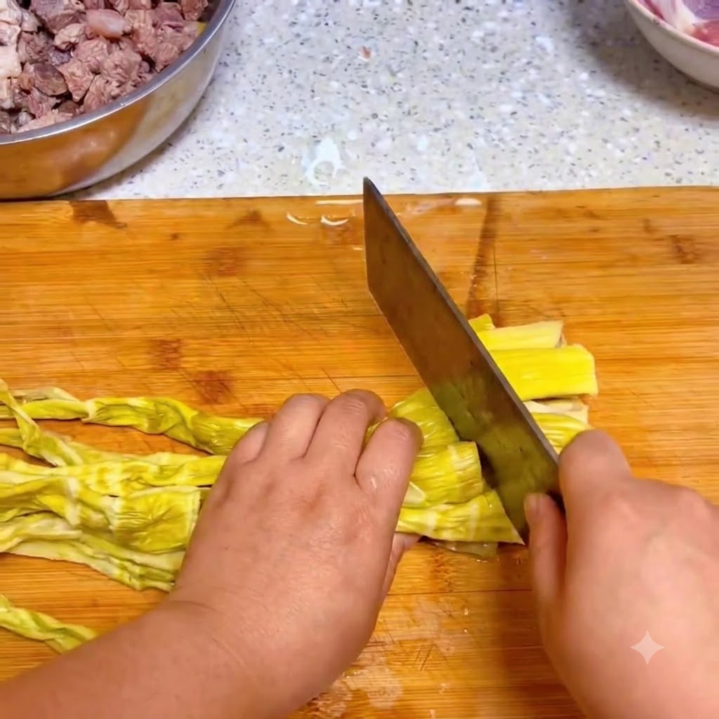 Un couteau de cuisine coupant des pousses de bambou jaunes réhydratées sur une planche à découper en bois.