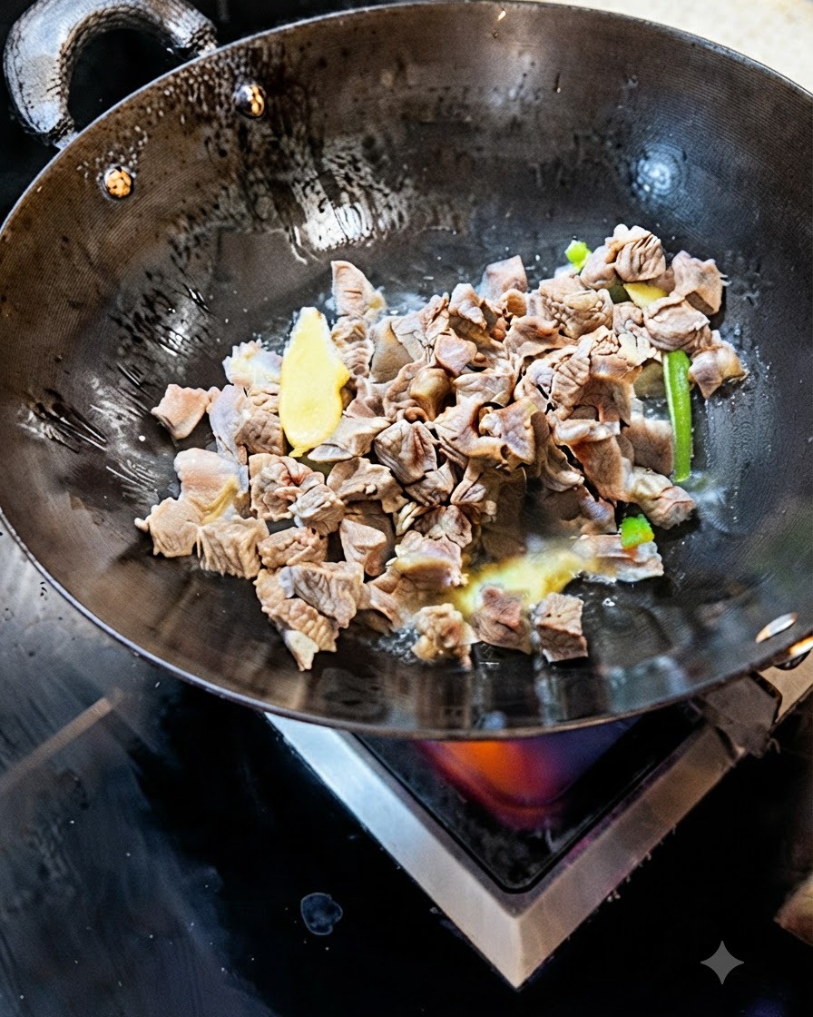 Des cubes de bœuf blanchis sautant dans un wok avec des tranches de gingembre et doignon vert.