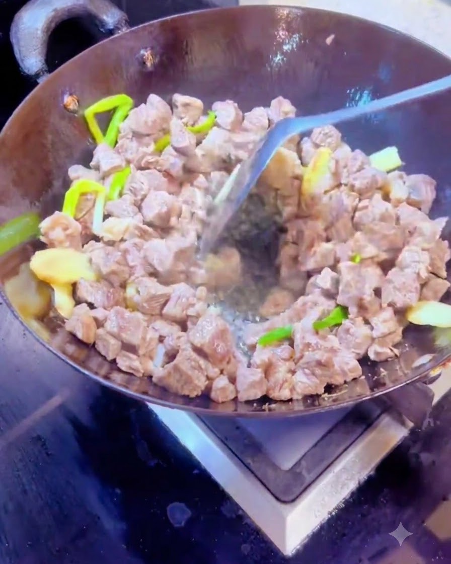 Mélange dépices sèches et de cubes de bœuf dans un wok chaud à laide dune spatule en métal.
