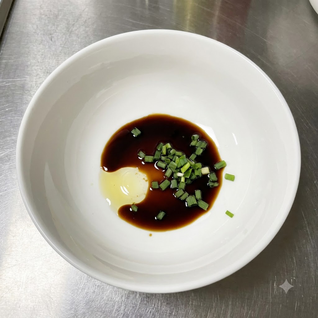 Un bol blanc contenant de la sauce soja claire, des oignons verts fraîchement coupés et une cuillerée de pâte dassaisonnement sur un comptoir en acier inoxydable.