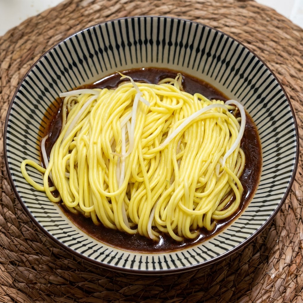 Une portion de nouilles jaunes chaudes et cuites reposant dans un bol en céramique à motifs sur une riche sauce marron foncé.