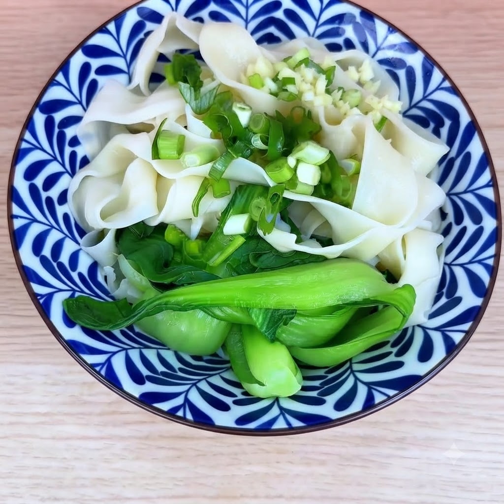 Un bol de nouilles cuites et de bok choy garni doignons verts hachés et dail émincé.