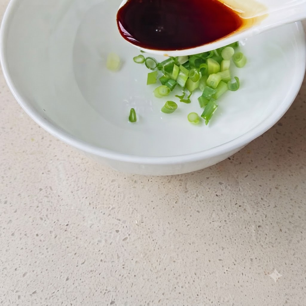 Une cuillère versant de la sauce soja foncée dans le bol contenant la ciboule.