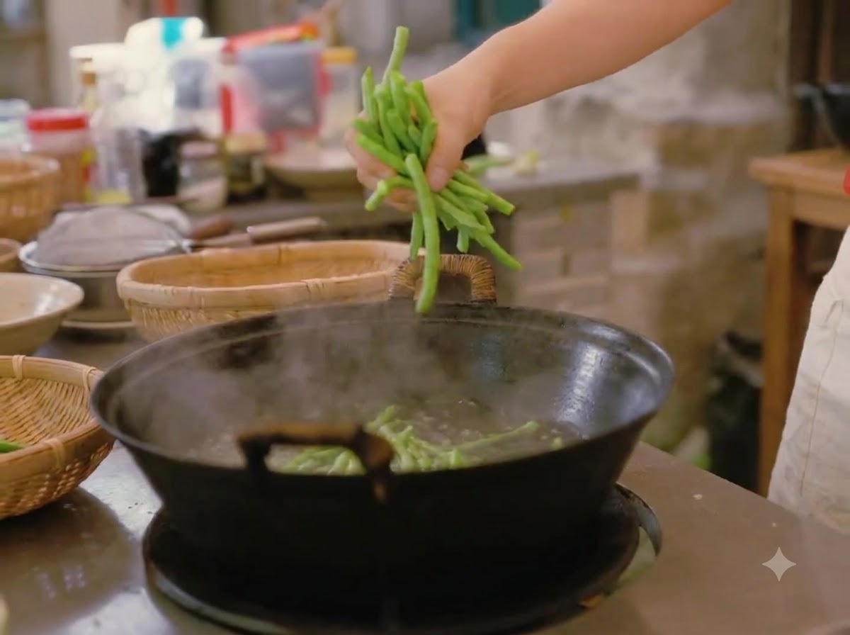 Une main plongeant une poignée de haricots verts frais dans un grand wok deau bouillante.