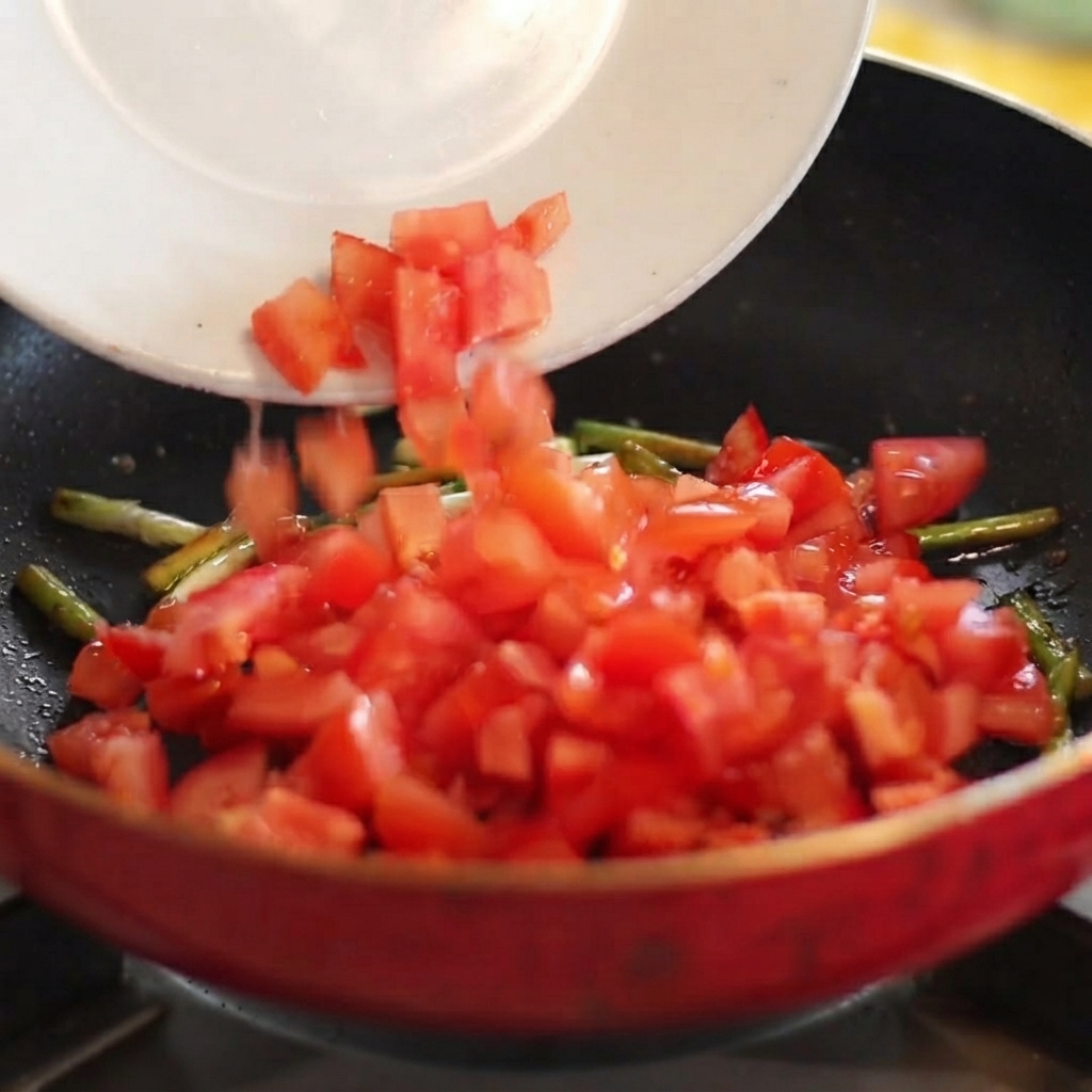 Tomates rouges en dés glissant dune assiette blanche vers une poêle chaude avec des oignons verts sautés.