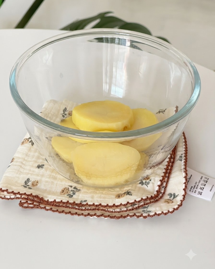 Des tranches de pommes de terre jaunes cuites à la vapeur reposant dans un bol en verre transparent sur un linge.