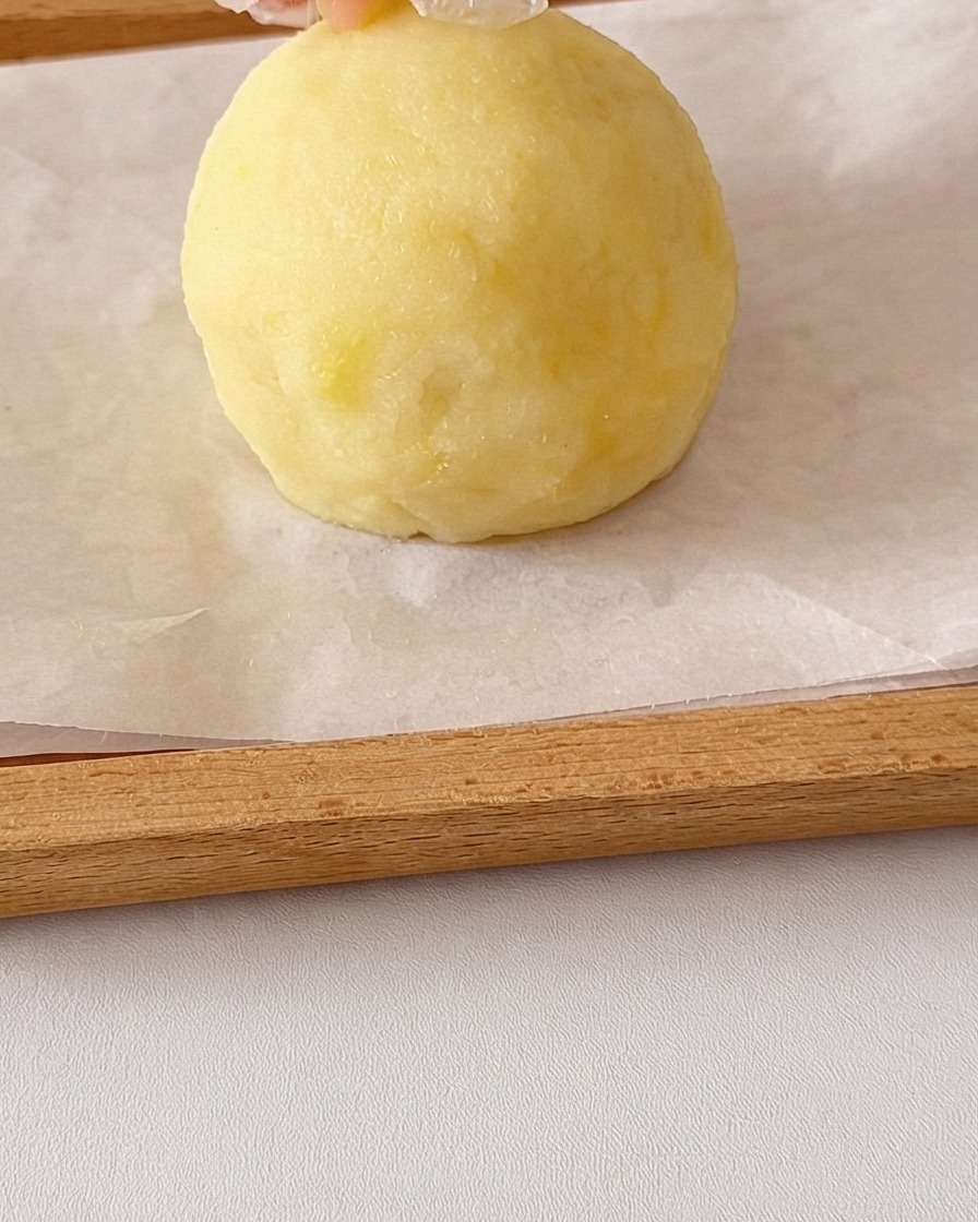 Une boule ronde de purée de pommes de terre lisse façonnée par des mains avec de petits morceaux de pommes de terre ajoutés sur le dessus pour les oreilles.