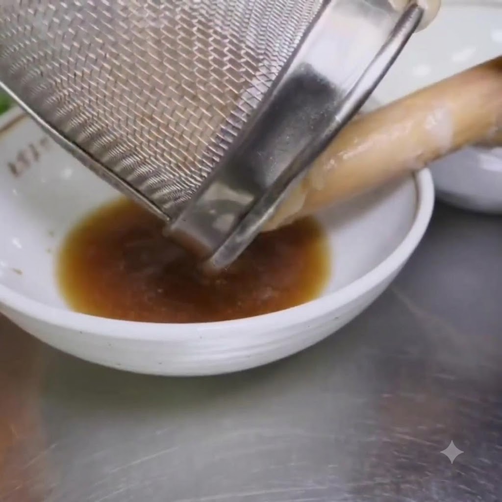 Des nouilles ramen bouillies versées dune passoire en mailles dans un bol contenant de lassaisonnement.