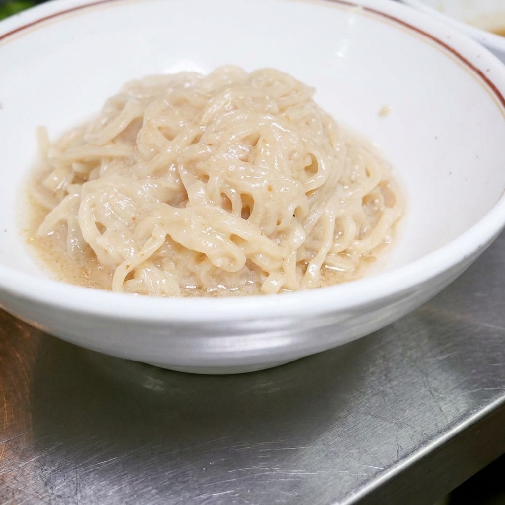 Des nouilles ramen cuites disposées proprement dans un bol blanc, prêtes à être mélangées avec la sauce.