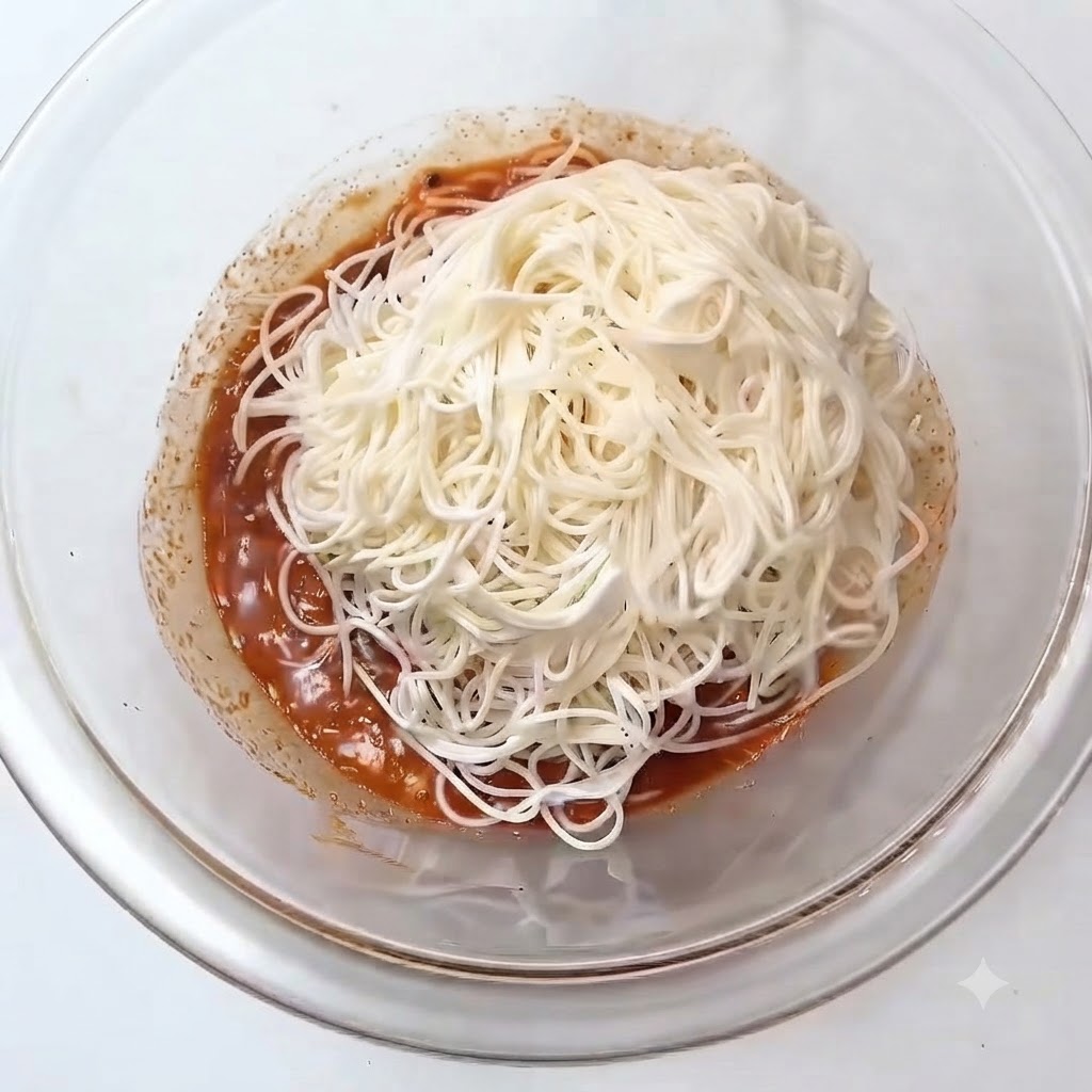 Un tas de nouilles somen blanches cuites placées sur la sauce rougeâtre à lintérieur dun bol mélangeur en verre.