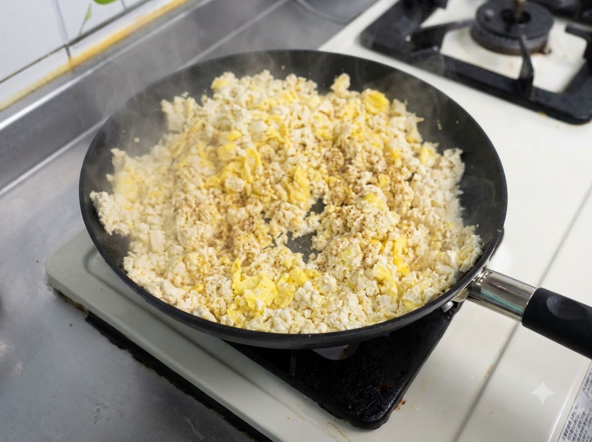 Une poêle remplie dun mélange dœufs brouillés et de tofu en train dêtre sauté avec de lassaisonnement saupoudré sur le dessus.