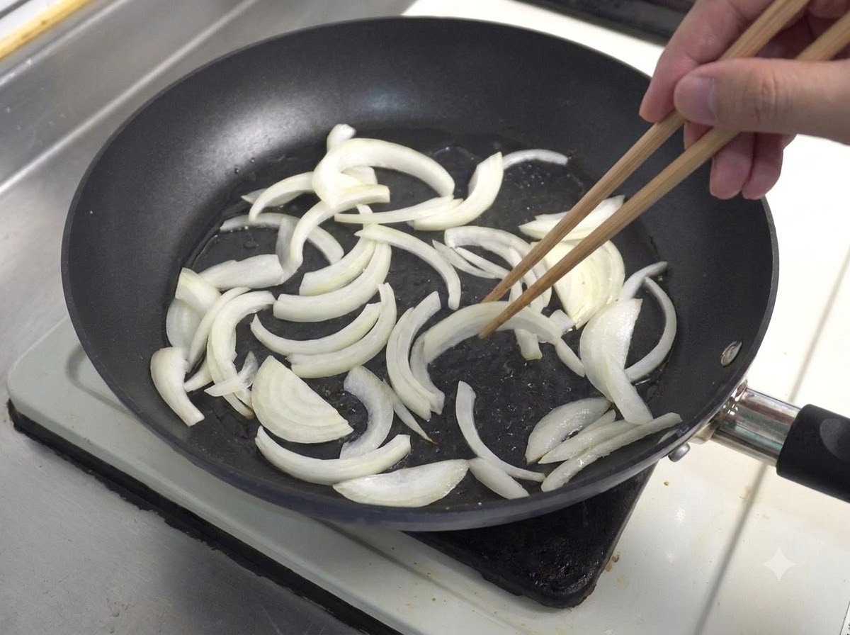 Des oignons blancs émincés sautés dans une poêle à laide de baguettes en bois.