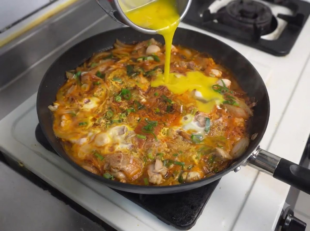 Versement dœufs battus supplémentaires dun récipient dans la poêle frémissante avec le poulet et le kimchi.