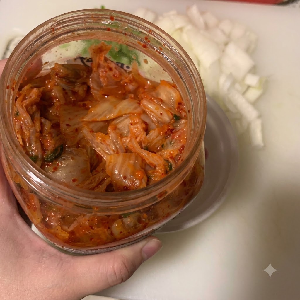 Du kimchi versé dans un petit bol blanc à laide dune cuillère, à côté dun récipient doignons hachés.