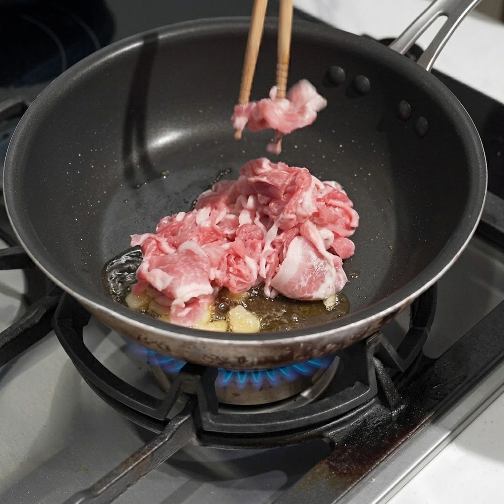 Porc cru finement émincé déposé dans une poêle avec de lhuile chaude et de lail frit à laide de baguettes.