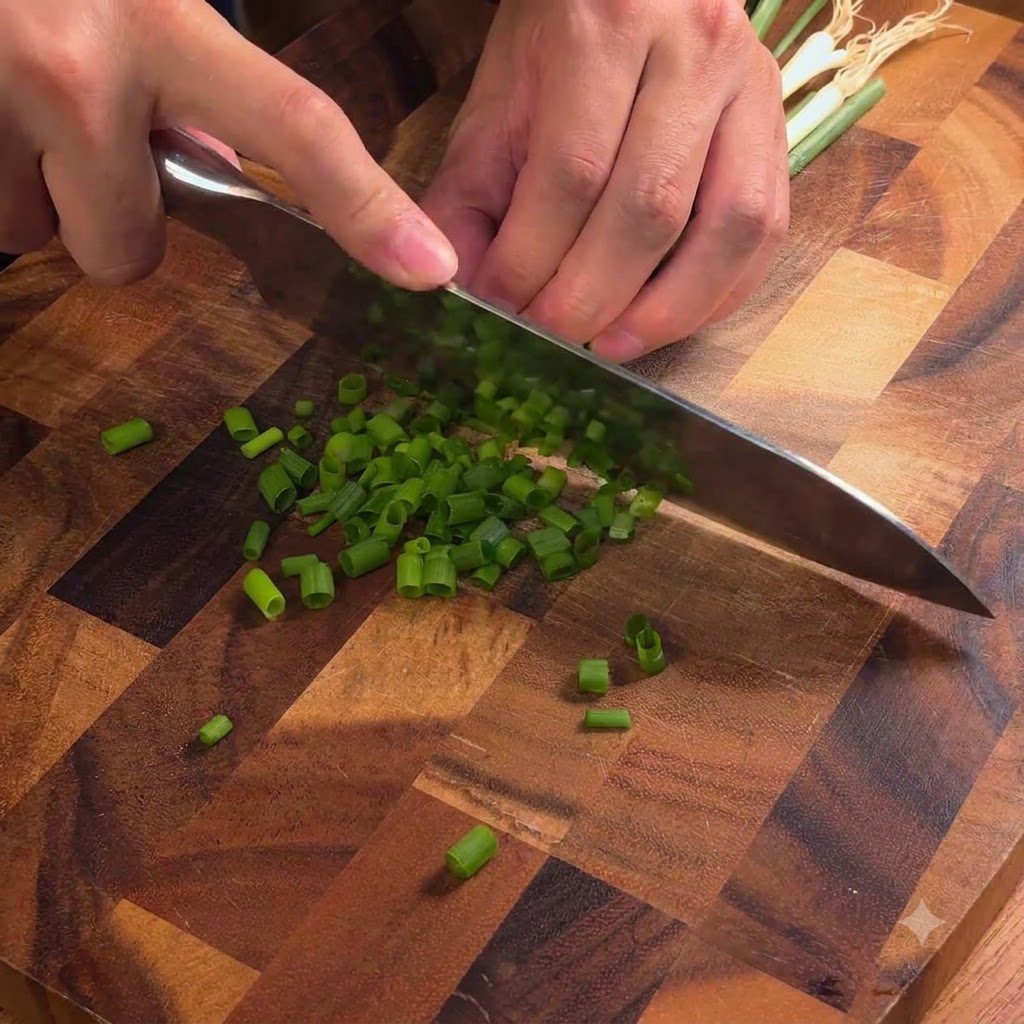 Un couteau de chef coupant des oignons verts frais en petits morceaux sur une planche à découper en bois.