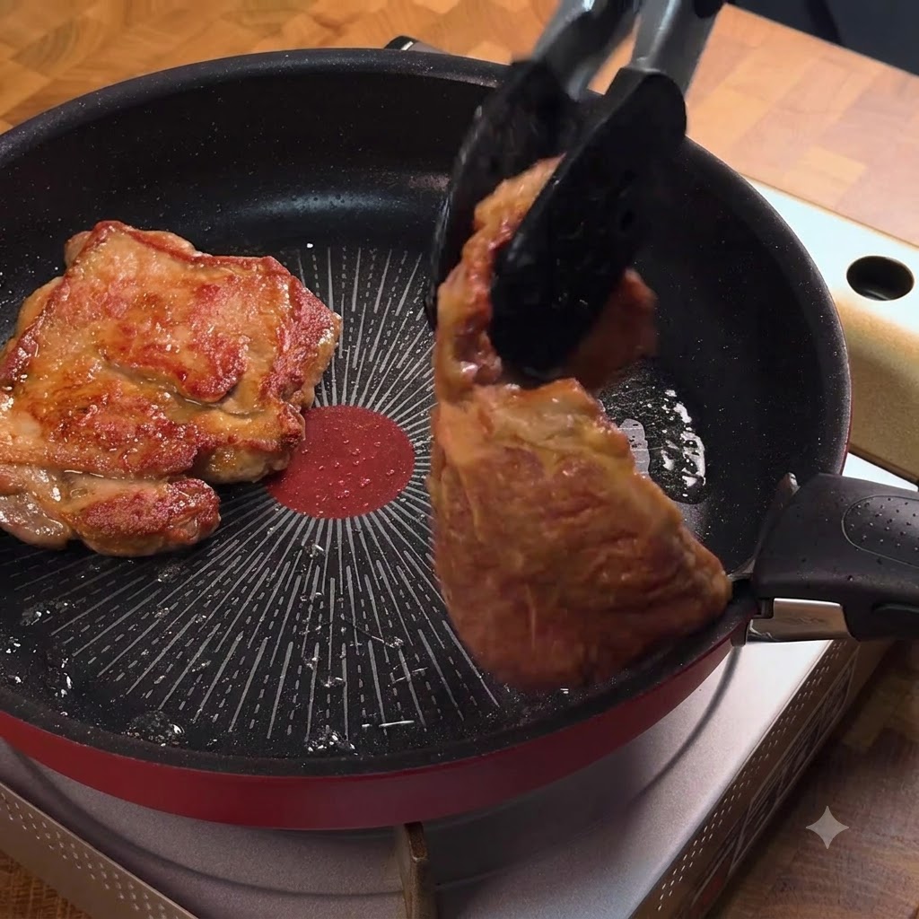Des pinces retournant une côte de porc dorée dans une poêle à frire.