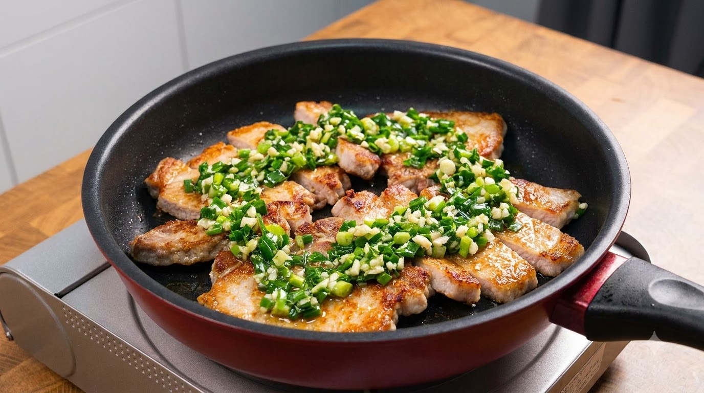 Tranches de côte de porc poêlées dorées à point, généreusement garnies doignons verts frais et dail émincé dans une poêle antiadhésive sombre