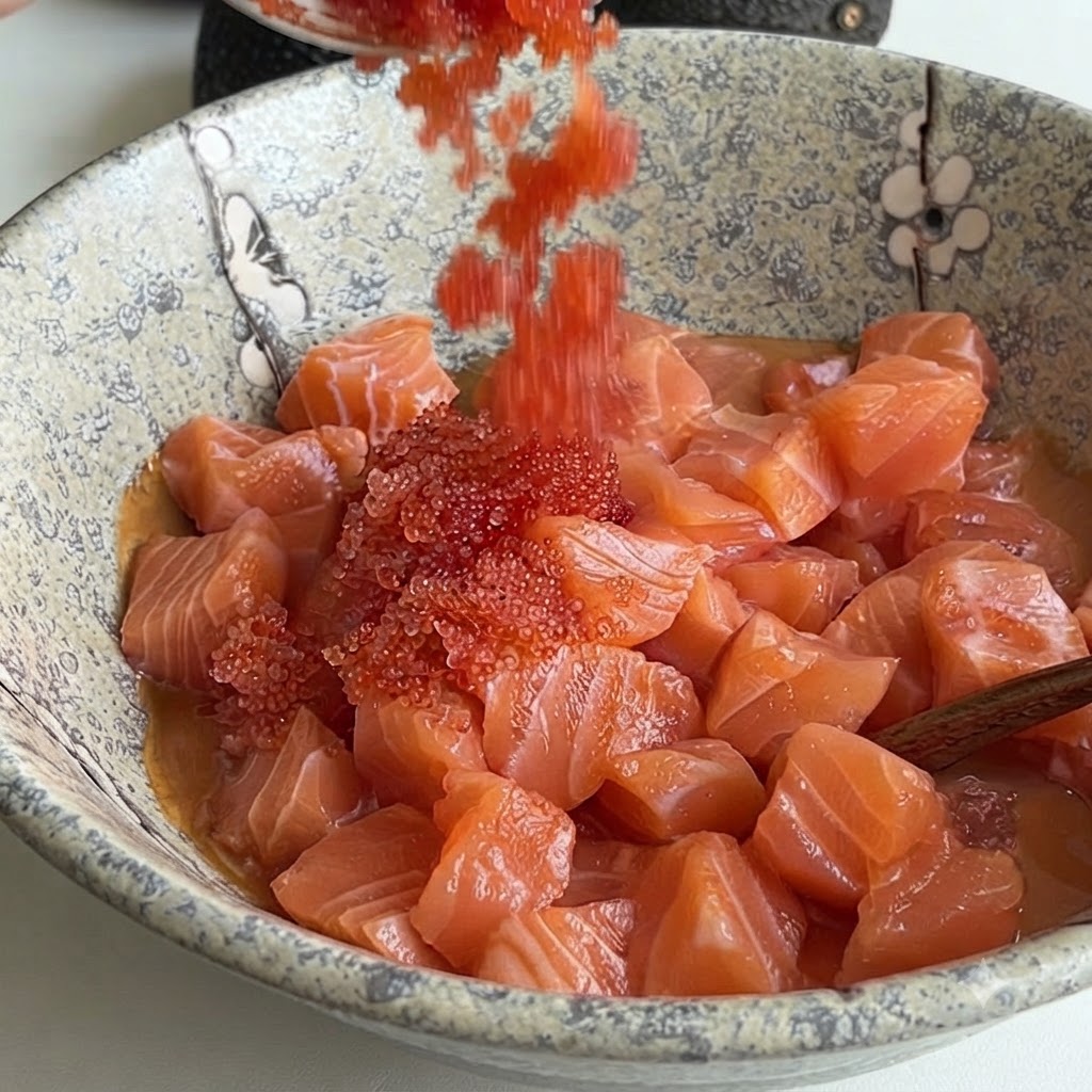 Des œufs de poisson rouge vif versés à laide dune cuillère dans un bol en céramique rempli de dés de saumon et de sauce.