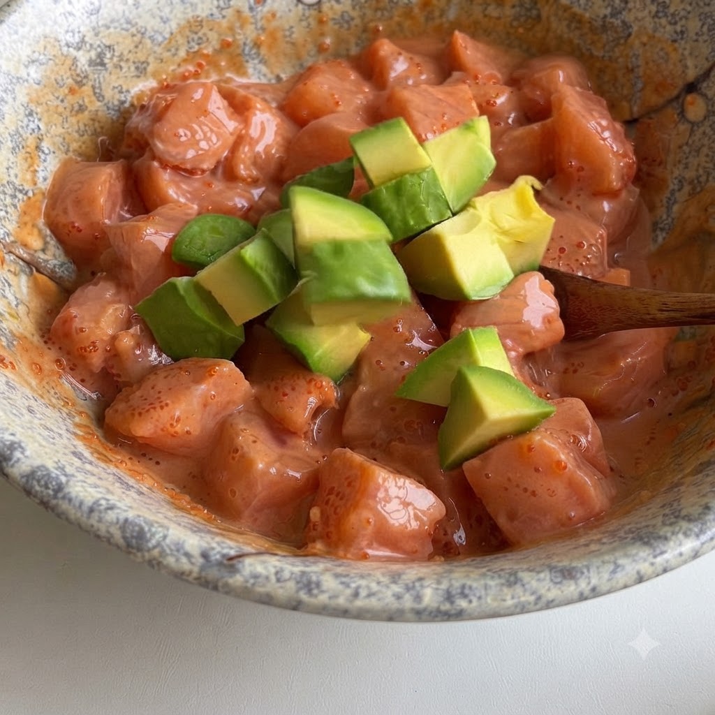Des cubes davocat vert incorporés délicatement dans un bol de cubes de saumon enrobés dune sauce rose crémeuse.