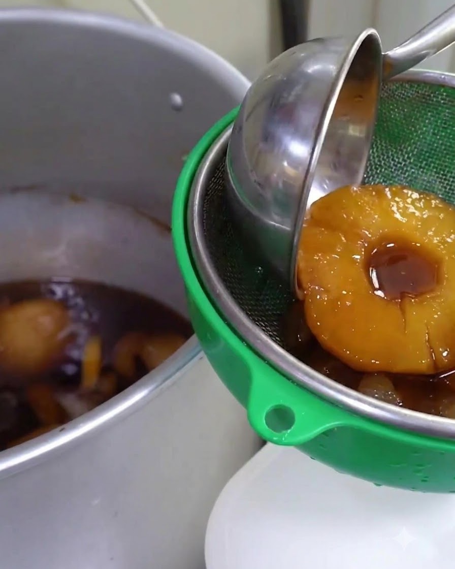 Sauce infusée aux fruits mijotée et filtrée à travers un tamis vert dans un grand récipient en métal.