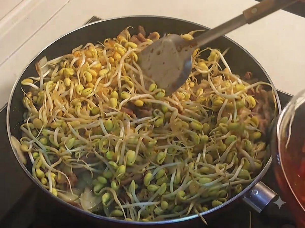 Une louche versant de la sauce rouge épicée sur une poêle remplie de pousses de soja jaune.