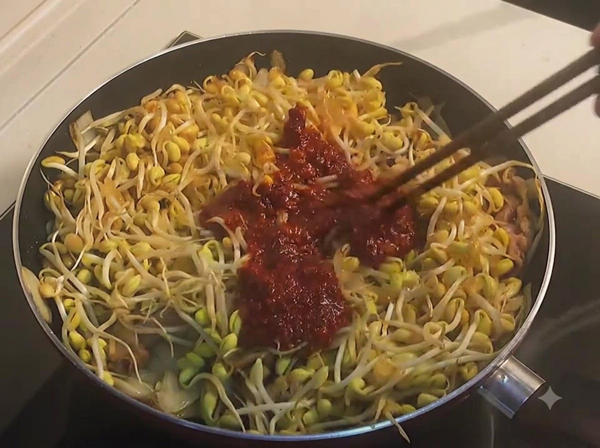 Des baguettes mélangeant des pousses de soja jaune et du bœuf avec une sauce épicée rouge foncée et épaisse dans une poêle.