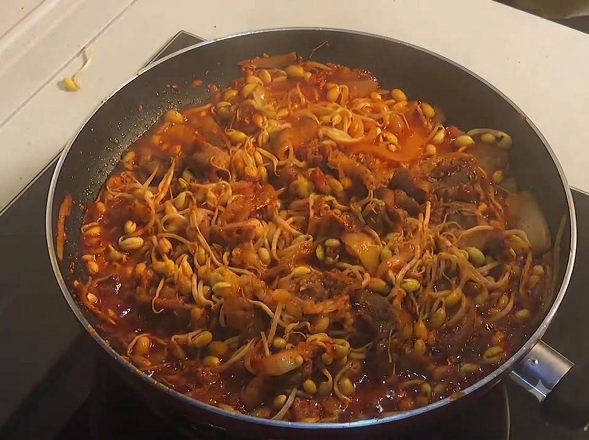 Une poêle pleine de bœuf épicé et de pousses de soja jaune entièrement cuits et frémissants dans une sauce rouge riche.