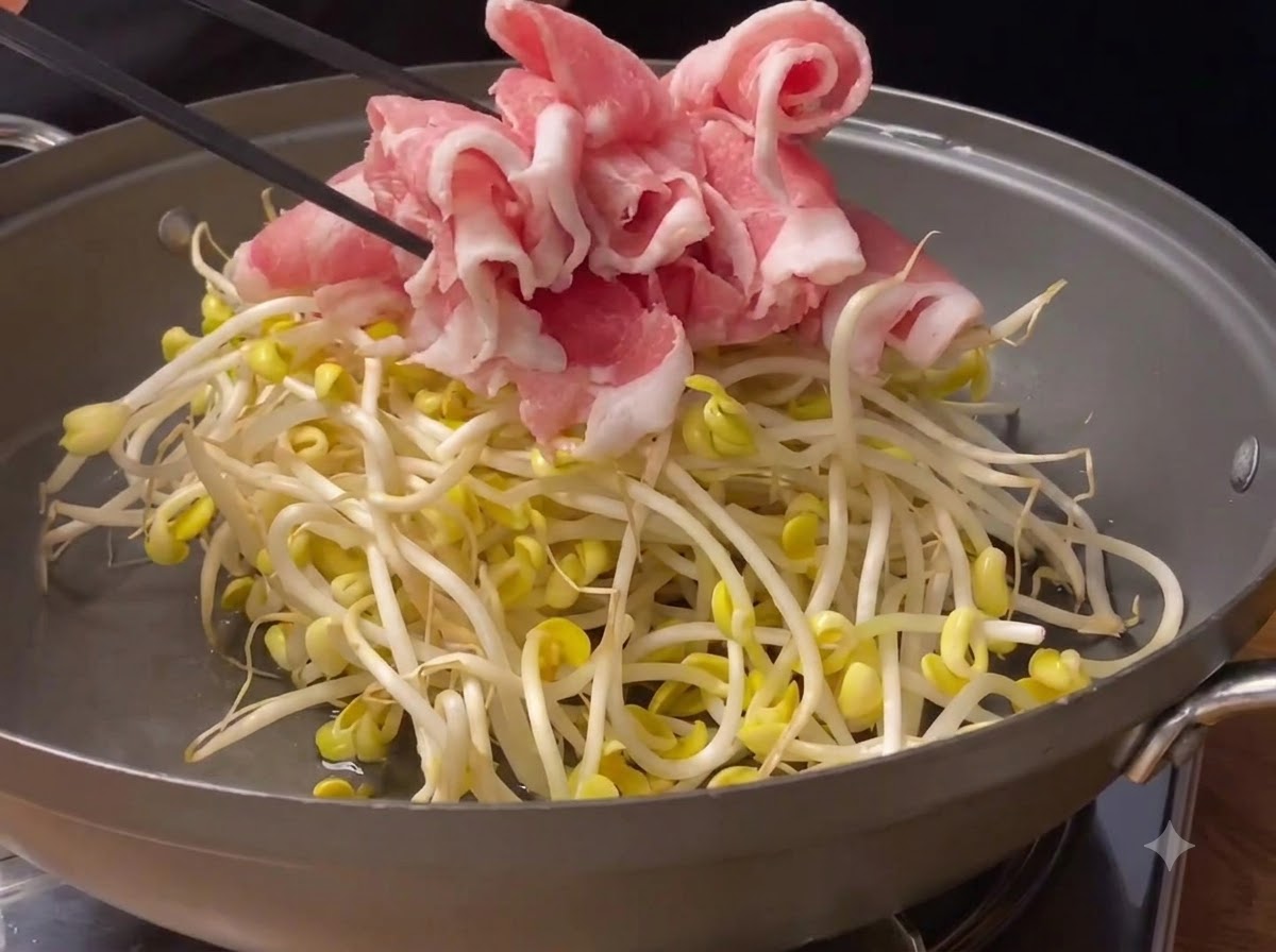 Rouleaux de porc roses finement tranchés placés sur le lit de germes de soja à lintérieur dune poêle.