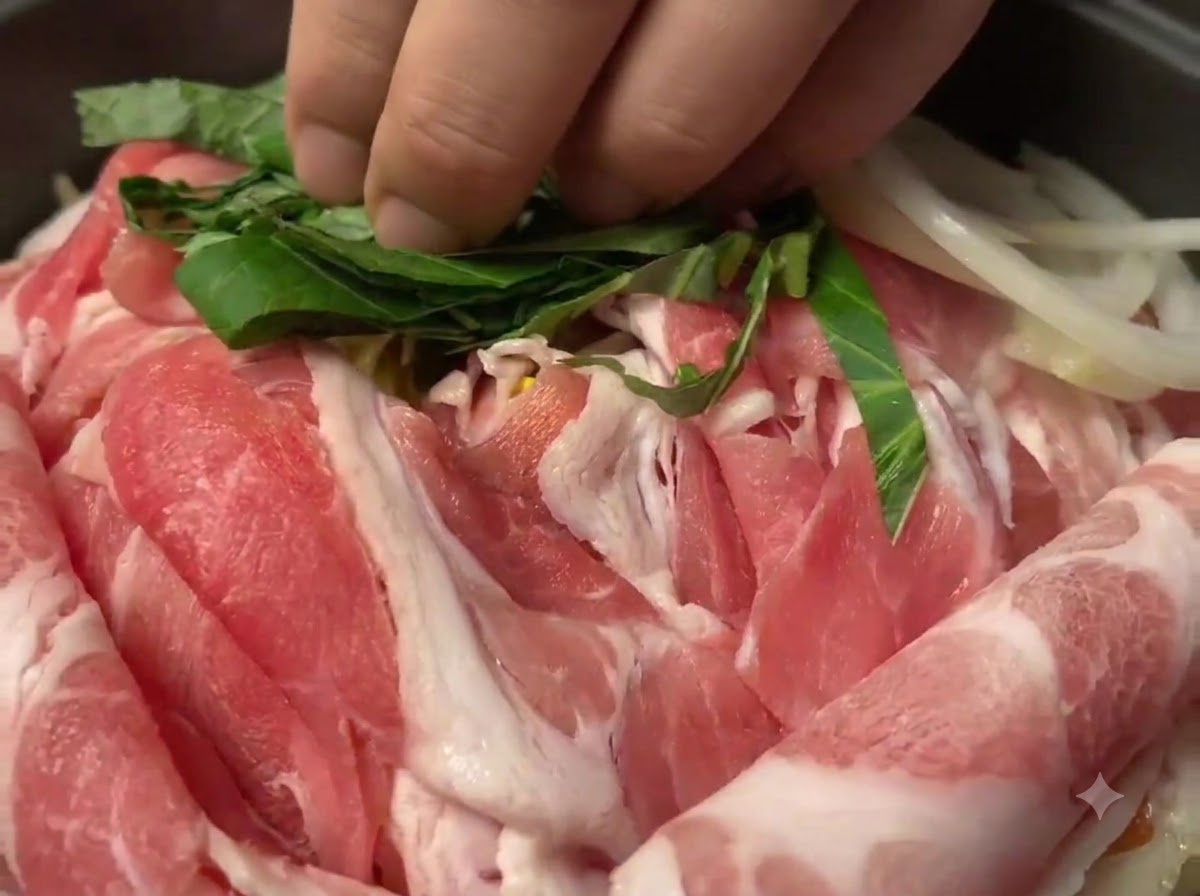 Feuilles de perilla vertes hachées dispersées sur les tranches de porc cru dans la poêle.