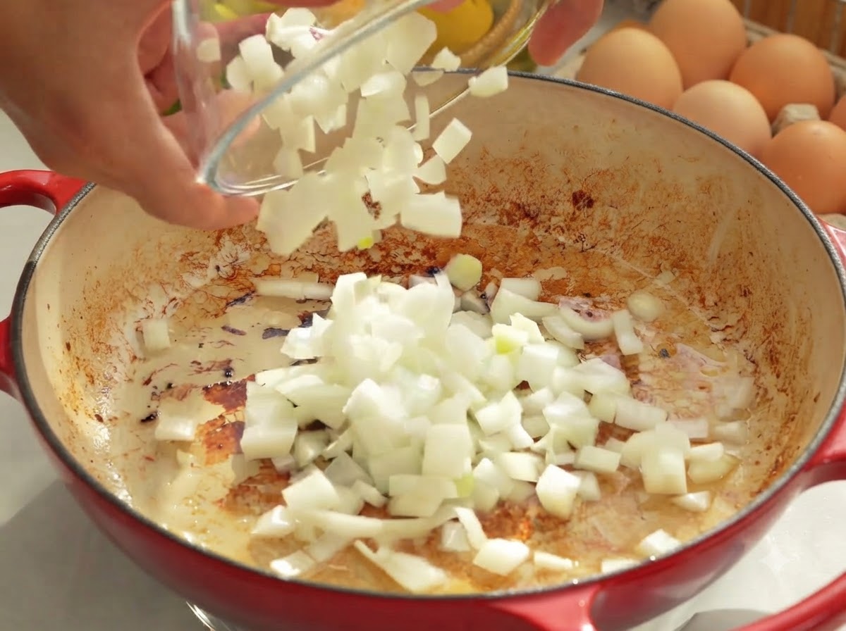 Des oignons hachés versés dun bol en verre dans une poêle chaude contenant de la graisse fondue.