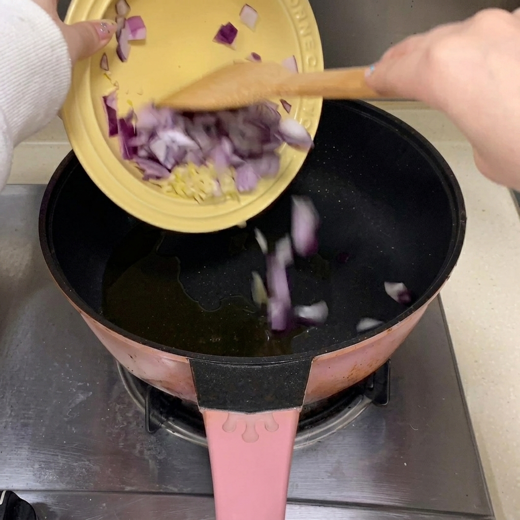 Morceaux dail émincé et doignon rouge tombant dans une poêle avec de lhuile de cuisson chaude.